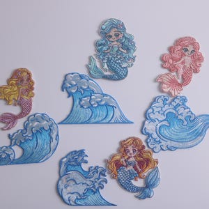 May include: Set of eight embroidered iron-on patches featuring mermaids and waves. The mermaids are in various colours, including pink, blue, and yellow. The waves are blue and white.