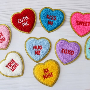 Könnte beinhalten: Neun Filz-Herz-Patches mit goldener Umrandung und gestickten Botschaften: "Cutie Pie", "Love You", "Kiss Me", "Sweet", "Hug Me", "XOXO", "You Rock", "True Love" und "Be Mine".