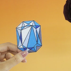 May include: A blue and white geometric embroidered patch shaped like a gemstone.