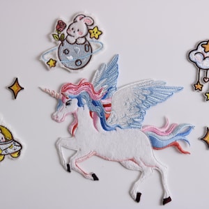 May include: A set of embroidered iron-on patches featuring a unicorn with wings, a bunny in a spaceship, a bunny on a planet, a cloud with stars, and stars.