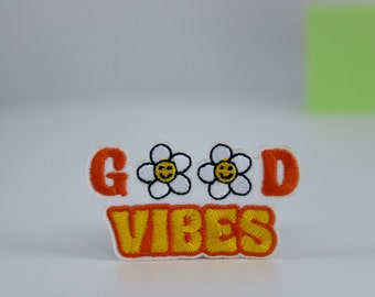 May include: Orange and yellow embroidered patch with the text "GOOD VIBES" and two white flowers with yellow smiley faces.