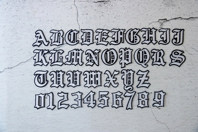 May include: White letters and numbers in a gothic font style on a white textured background. The letters are A through Z and the numbers are 0 through 9.