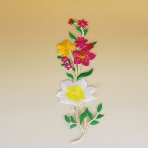 May include: A colorful embroidered flower patch with white, yellow, pink, and green accents. The patch features a variety of flowers and leaves, perfect for adding a touch of whimsy to clothing or crafts.