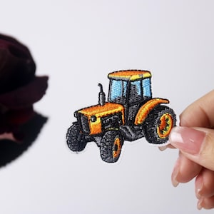 May include: An embroidered iron-on patch of a yellow tractor with black wheels and a blue windshield.