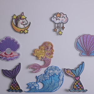 May include: A set of eight embroidered iron-on patches featuring a mermaid, a seashell, a unicorn, a cloud with stars, and three mermaid tails. The patches are colorful and whimsical.