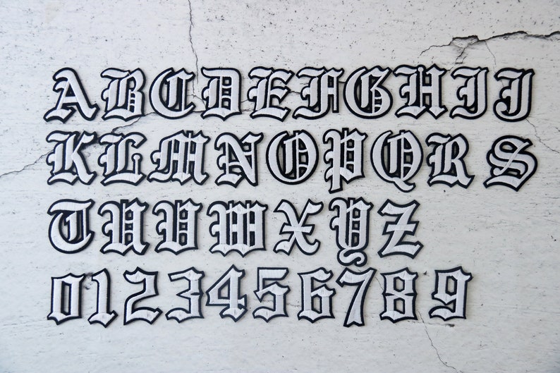 May include: White letters and numbers in a black outline, in a gothic font style. The letters are A through Z and the numbers are 0 through 9.