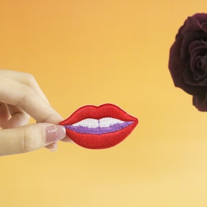 May include: A red embroidered patch of a smiling mouth with white teeth and a purple outline.