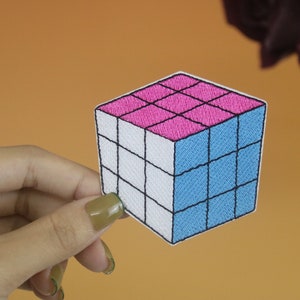 May include: A pink and blue embroidered patch shaped like a Rubik's Cube.