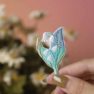 Op de afbeelding: Een geborduurde lelietje-van-dalen-bloemenpatch met groene en blauwe bladeren.