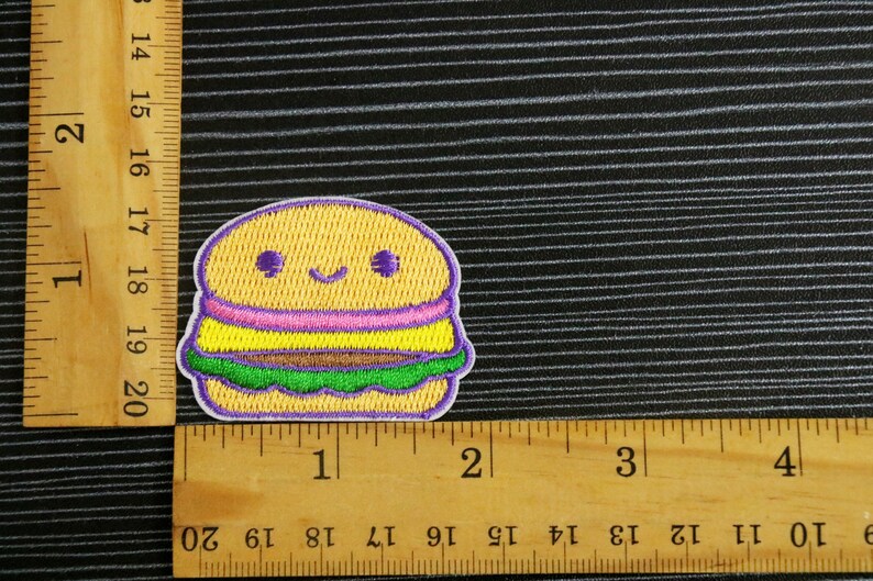 May include: A yellow, purple, pink, and green embroidered iron-on patch of a smiling cartoon hamburger. The patch is about 1.5 inches wide.