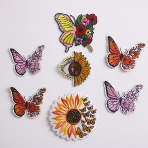 May include: Assortment of embroidered iron-on patches featuring butterflies, sunflowers, and an eye design. The patches are colorful and detailed, perfect for adding a unique touch to clothing, bags, or other accessories.