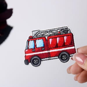 May include: Red and white embroidered iron-on patch of a fire truck with a ladder on top.