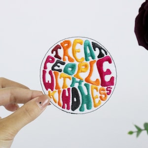 May include: A round embroidered patch with the text "Treat People With Kindness" in a colourful, retro font.