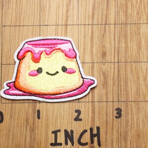 Peut inclure: Un patch brod&eacute; thermocollant repr&eacute;sentant un pudding en dessin anim&eacute; avec un visage souriant. Le patch mesure environ 5 cm de large.