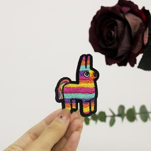 May include: A colorful embroidered iron-on patch of a pinata shaped like a llama. The pinata is striped with pink, orange, yellow, green, and blue.