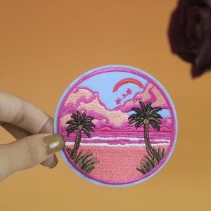 May include: A pink and blue embroidered patch depicting a sunset scene with two palm trees, a crescent moon, and stars. The patch is circular and has a white border.