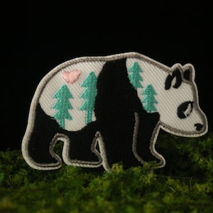 May include: Embroidered iron-on patch featuring a black and white panda bear with a pink heart and green pine trees on its back.