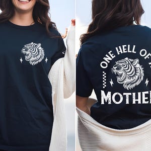 May include: A navy blue t-shirt with a white tiger graphic on the front and the text "ONE HELL OF A MOTHER" with a white tiger graphic on the back.