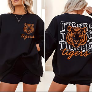May include: Black sweatshirt with an orange tiger graphic and the word "tigers" in orange script. The back of the sweatshirt features a larger tiger graphic and the word "tigers" repeated in a block letter design.