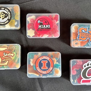 May include: Six clear plastic containers filled with colorful gummy candies. Each container has a different college logo sticker on the front. The logos are for the University of Colorado Buffaloes, Miami RedHawks, Syracuse Orange, Louisville Cardinals, Illinois Fighting Illini, and the University of California, Berkeley Golden Bears.