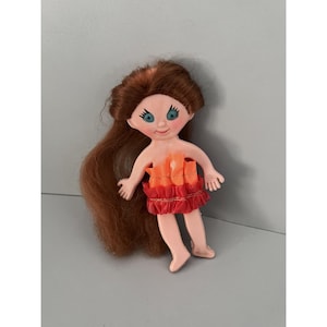 May include: A vintage doll with long auburn hair and blue eyes. The doll is wearing a red and orange ruffled skirt and top. The doll's skin is a light pink color.
