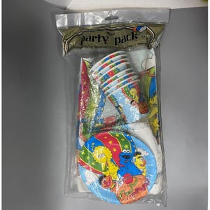 May include: A sealed party pack featuring Sesame Street characters. The pack includes cups, plates, and a tablecloth, all adorned with colorful illustrations of Big Bird, Cookie Monster, and Elmo. The packaging reads "Regal Party Pack".
