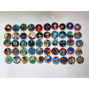 May include: A collection of Power Rangers pogs, each featuring a different character or image from the series. The pogs are round with colorful designs and text, including character names and action phrases.