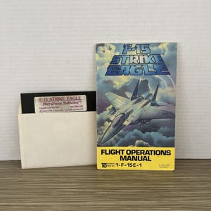 May include: An F-15 Strike Eagle Flight Operations Manual and a 5.25-inch floppy disk. The manual features an illustration of a fighter jet against a cloudy sky. The disk is labeled "F-15 Strike Eagle MicroProse Software".