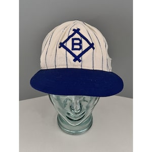 May include: Vintage baseball cap with a cream-colored crown featuring blue pinstripes and a blue brim. The front displays a blue diamond with the letter "B" inside. A classic sports accessory.