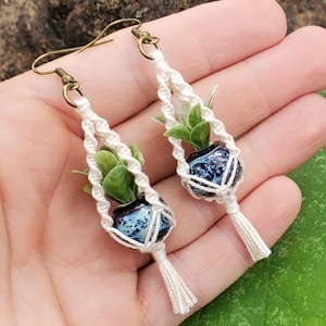 May include: A pair of white macrame earrings with blue and white ceramic pots and green faux plants.