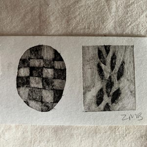 Puede incluir: Una pequeña obra de arte rectangular con dos diseños en escala de grises. Uno es un óvalo con un patrón tejido, y el otro es un panel rectangular con una disposición de hojas. Las iniciales del artista, ZMB, son visibles.