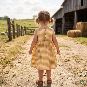 May include: A young child wearing a sleeveless, yellow and white gingham dress with brown sandals stands on a dirt path. The dress has a button-up back. The child is facing away from the camera, looking towards a wooden fence and barn in the background.