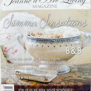 May include: Magazine cover titled "Jeanne d'Arc Living" with "Summer Sensations" in script. A decorative bowl with handles is filled with small beige spheres and lace. The cover includes text about homes and gardens.