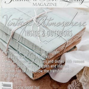 May include: A stack of vintage magazines tied with twine. The cover features the text "Vintage Atmosphere Inside & Outdoors" and the magazine title "Jeanne d'Arc Living." Additional text includes article topics and the phrase "dream homes of this spring."