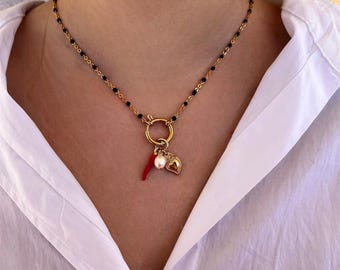 以下が含まれることがあります： 黒いビーズチェーンと、赤い唐辛子、真珠、金のハートのチャームが付いた金のチェーンネックレスです。