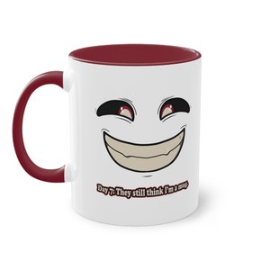 May include: White ceramic mug with a red rim and handle. The mug features a cartoon face with a wide smile and red eyes. The text "Day 7: They still think I'm a mug." is printed on the bottom of the mug.