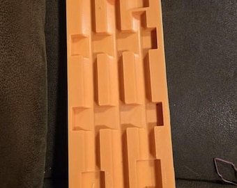 May include: An orange rectangular mold with a series of rectangular and square cavities. The mold is made of a flexible material and is likely used for creating multiple small objects. The design suggests a crafting or DIY theme.