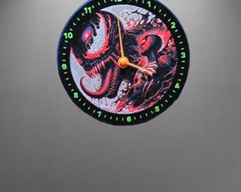 May include: Round wall clock featuring a comic book style illustration of a red and black monster with a long tongue. The clock has a black bezel with green glowing numbers and orange hands.
