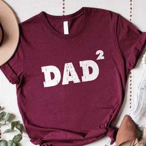 May include: Burgundy t-shirt with white text that reads "DAD²".