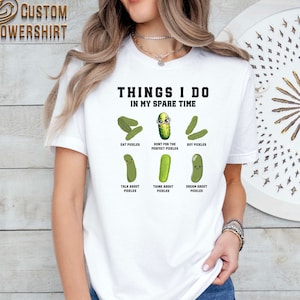 May include: White t-shirt with the text "Things I do in my spare time" and a series of cartoon pickles with text describing activities related to pickles, such as "Eat Pickles", "Hunt for the Perfect Pickles", "Buy Pickles", "Talk About Pickles", "Think About Pickles", and "Dream About Pickles".