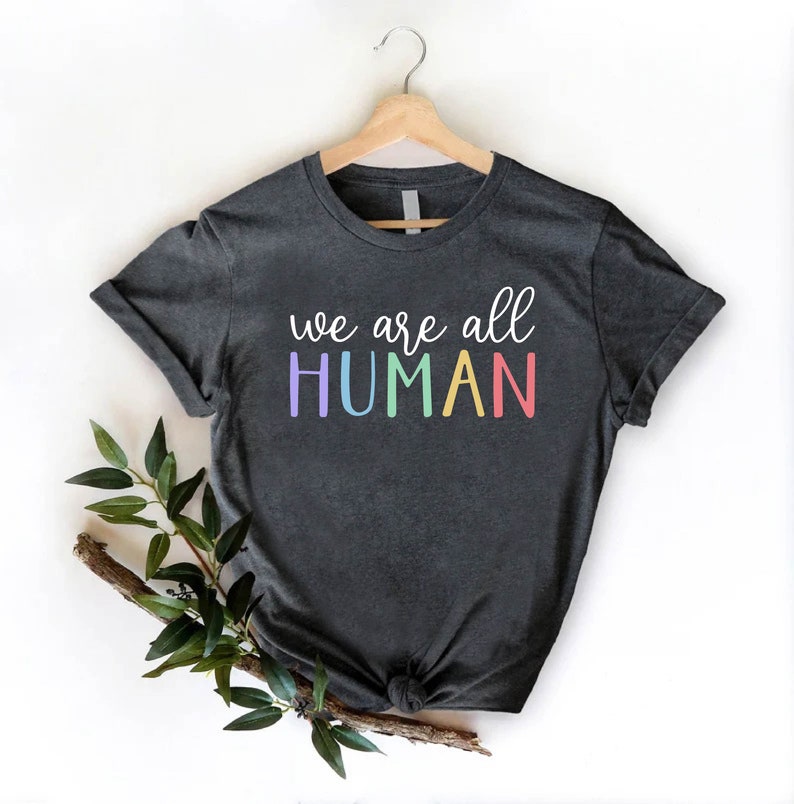 Puede incluir: Una camiseta gris oscuro con el texto "we are all HUMAN" en colores arco&iacute;ris.