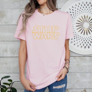 a woman wearing a pink t - shirt that says stop wars