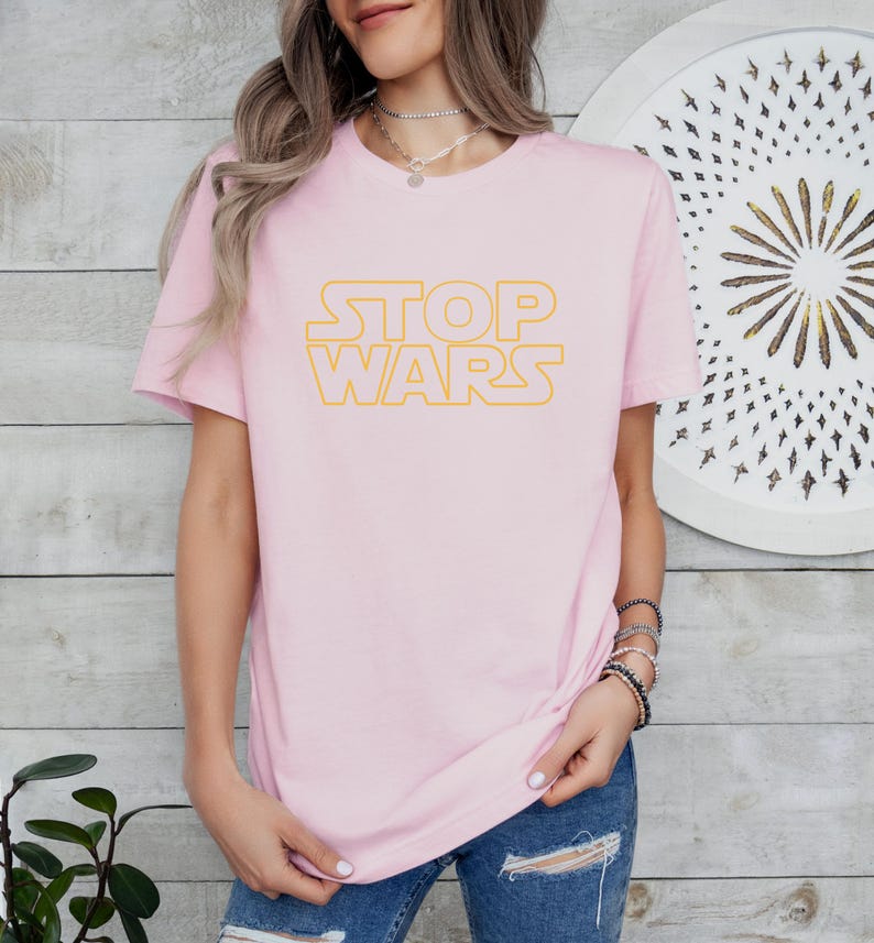 a woman wearing a pink t - shirt that says stop wars