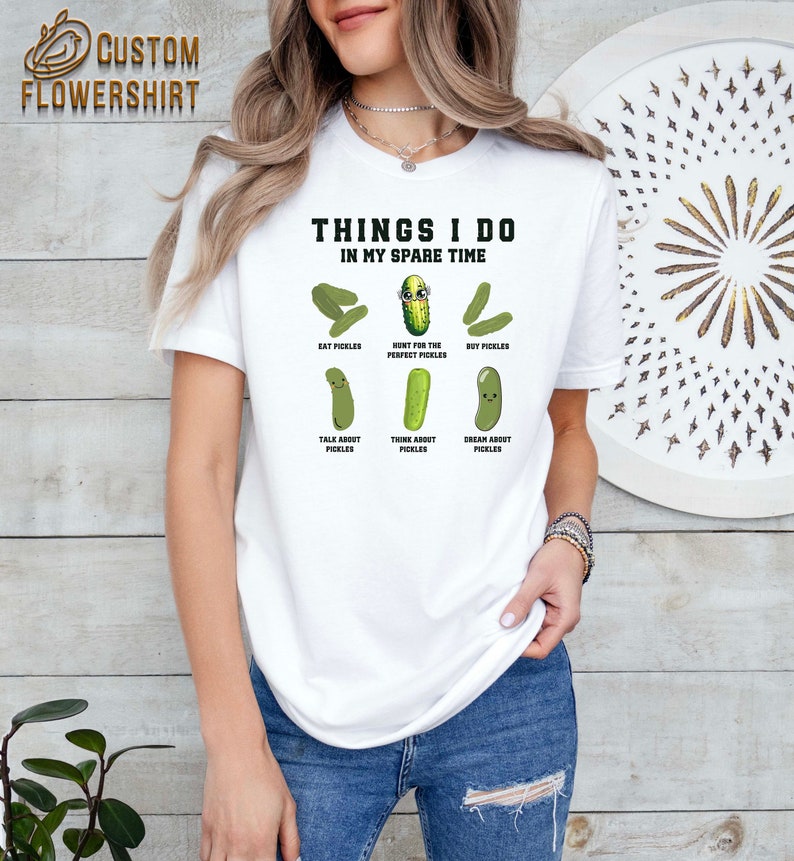 May include: White t-shirt with the text "Things I do in my spare time" and a series of cartoon pickles with text describing activities related to pickles, such as "Eat Pickles", "Hunt for the Perfect Pickles", "Buy Pickles", "Talk About Pickles", "Think About Pickles", and "Dream About Pickles".