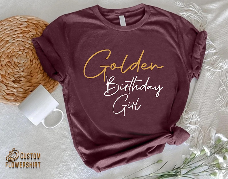 May include: Burgundy t-shirt with the text "Golden Birthday Girl" in gold and white lettering.