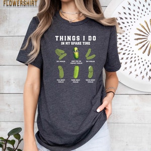 May include: A dark grey t-shirt with the text "Things I do in my spare time" and a cartoon pickle with the text "Hunt for the perfect pickles". The shirt also features other cartoon pickles with the text "Eat pickles", "Buy pickles", "Talk about pickles", "Think about pickles", and "Dream about pickles".