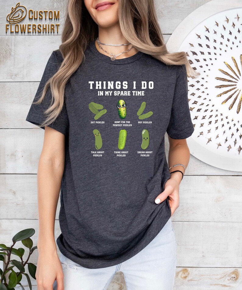 May include: A dark grey t-shirt with the text "Things I do in my spare time" and a cartoon pickle with the text "Hunt for the perfect pickles". The shirt also features other cartoon pickles with the text "Eat pickles", "Buy pickles", "Talk about pickles", "Think about pickles", and "Dream about pickles".