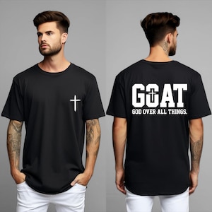 May include: Black t-shirt with a white cross on the front and the text "GOAT GOD OVER ALL THINGS" on the back. The shirt is a crew neck style and is being modeled.