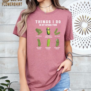 May include: A pink t-shirt with the text "Things I do in my spare time" and a series of cartoon pickles with text describing activities related to pickles. The text includes "Eat Pickles", "Hunt for the Perfect Pickles", "DIY Pickles", "Talk About Pickles", "Think About Pickles", and "Dream About Pickles".