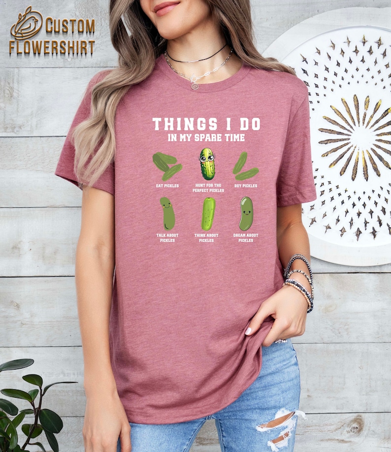 May include: A pink t-shirt with the text "Things I do in my spare time" and a series of cartoon pickles with text describing activities related to pickles. The text includes "Eat Pickles", "Hunt for the Perfect Pickles", "DIY Pickles", "Talk About Pickles", "Think About Pickles", and "Dream About Pickles".